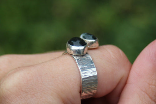 Close-up of a hand wearing two silver rings with a blurred green background